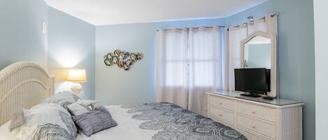 A bedroom with a bed, dresser, television, and decorative wall art.