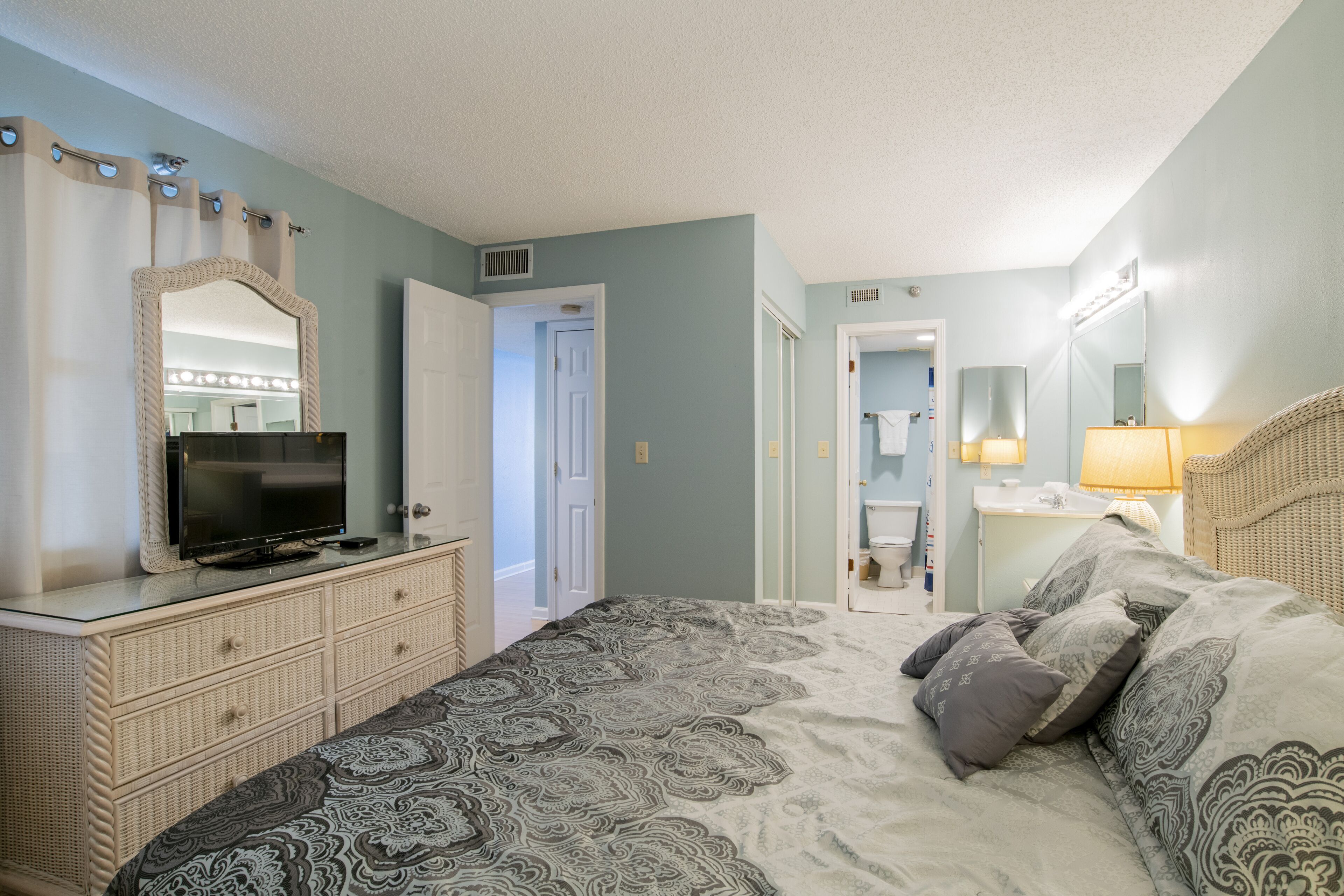 Een slaapkamer met een bed, een dressoir, een spiegel en een badkamer zichtbaar door een open deur.