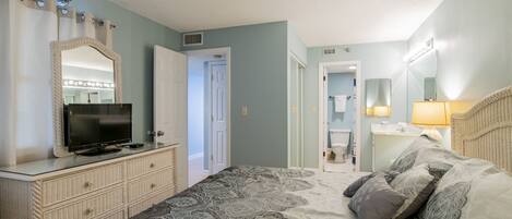 Een slaapkamer met een bed, een dressoir, een spiegel en een badkamer zichtbaar door een open deur.