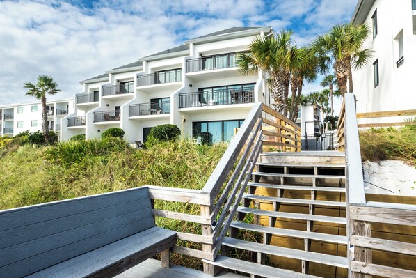 A multi-story building with balconies, wooden steps, and palm trees.