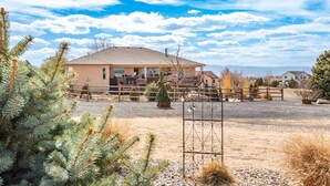 Uma casa no estilo rancho com um quintal cercado, uma arena coberta para equitação e montanhas ao fundo.