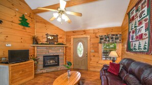 A cozy cabin interior with a fireplace, wooden walls, a leather sofa, and a ceiling fan. - ER307- Eagle's View- Great location- Close to town (Pigeon Forge)