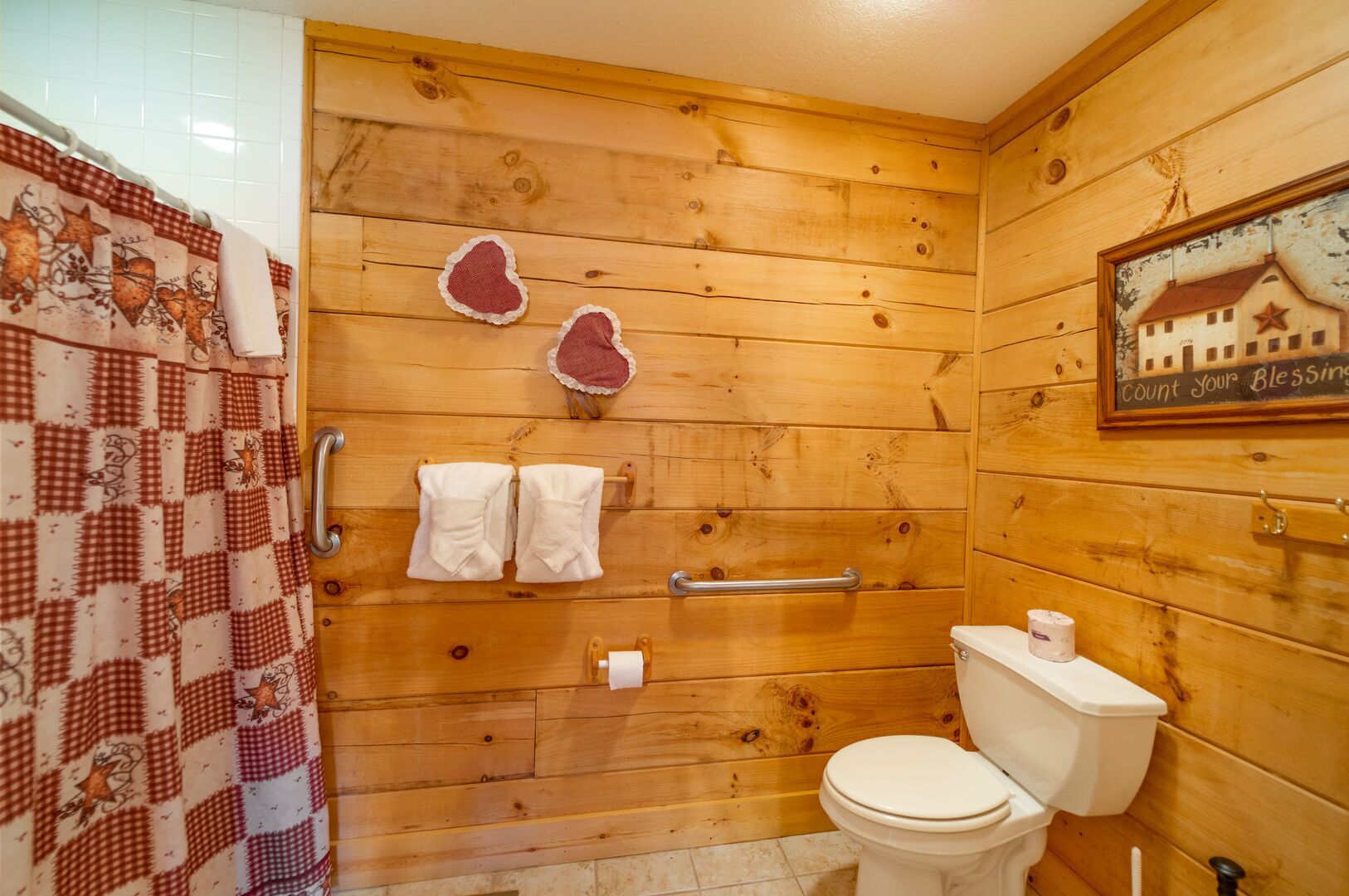 Une salle de bain en bois avec un rideau de douche, deux serviettes, des toilettes et un tableau encadré au mur.