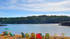 A lakeside view with a row of colorful Adirondack chairs facing the water, a small play structure, and a forested shoreline in the background. - Comfy Ledges Lakefront Condo--quiet cove, boat slip included! (Osage Beach)