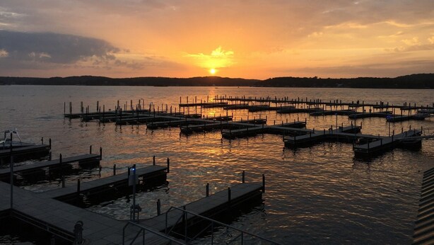 A marina with multiple docks extending into calm waters during sunset. - Comfy Ledges Lakefront Condo--quiet cove, boat slip included! (Osage Beach)