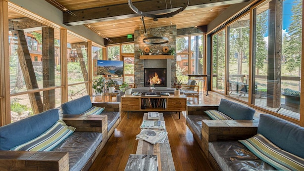 A spacious room with a fireplace, wooden furniture, and large windows offering a view of the outdoors.