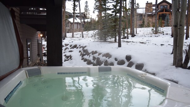 A hot tub with a view of a snowy landscape and a lodge in the background.