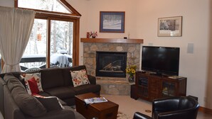 A living room with a stone fireplace, a television, a sofa, and a large window with curtains.