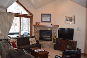 A living room with a stone fireplace, a television, a sofa, and a large window with curtains.