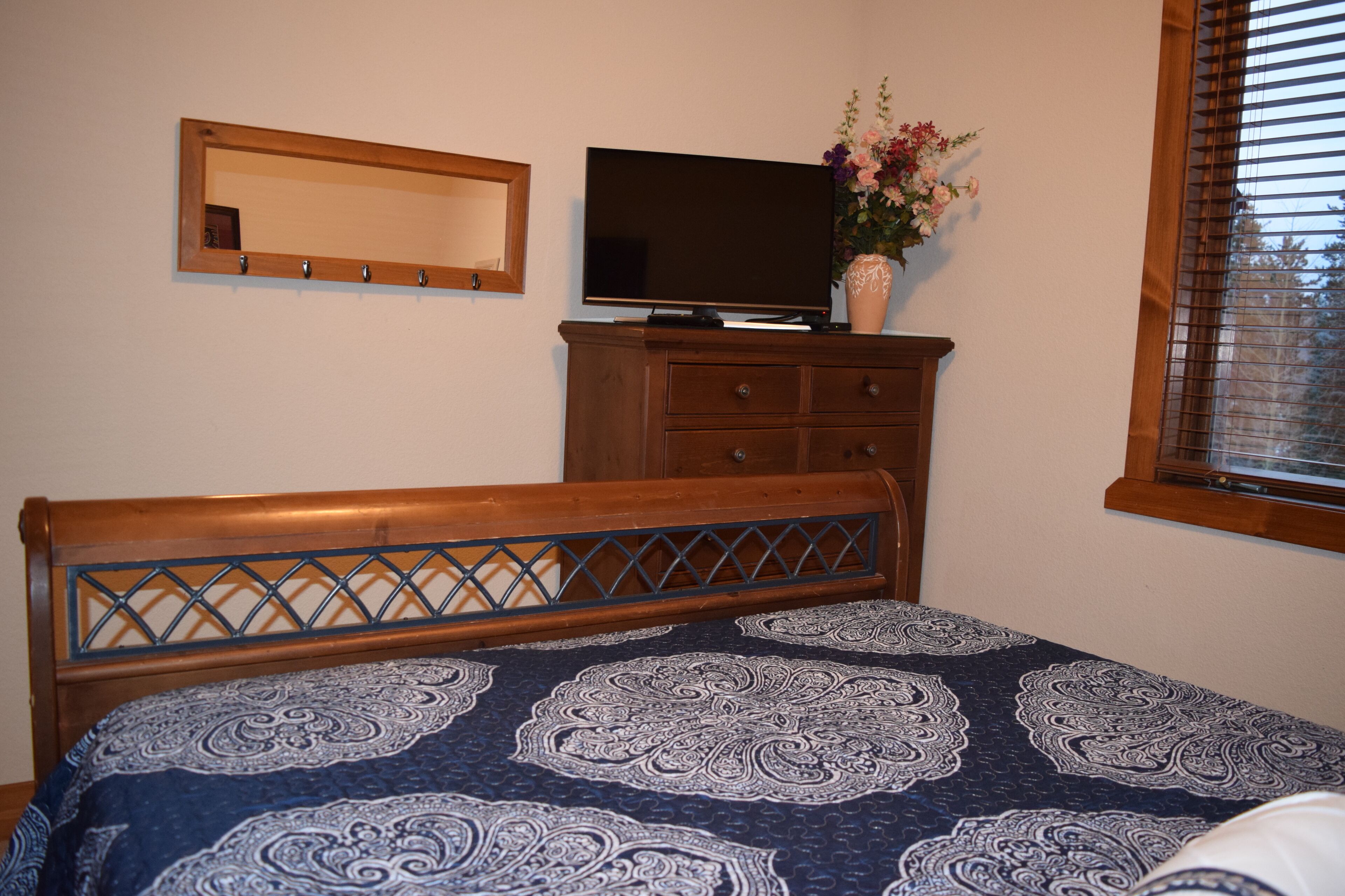 A bedroom with a bed, a dresser, a television, and a window with blinds.
