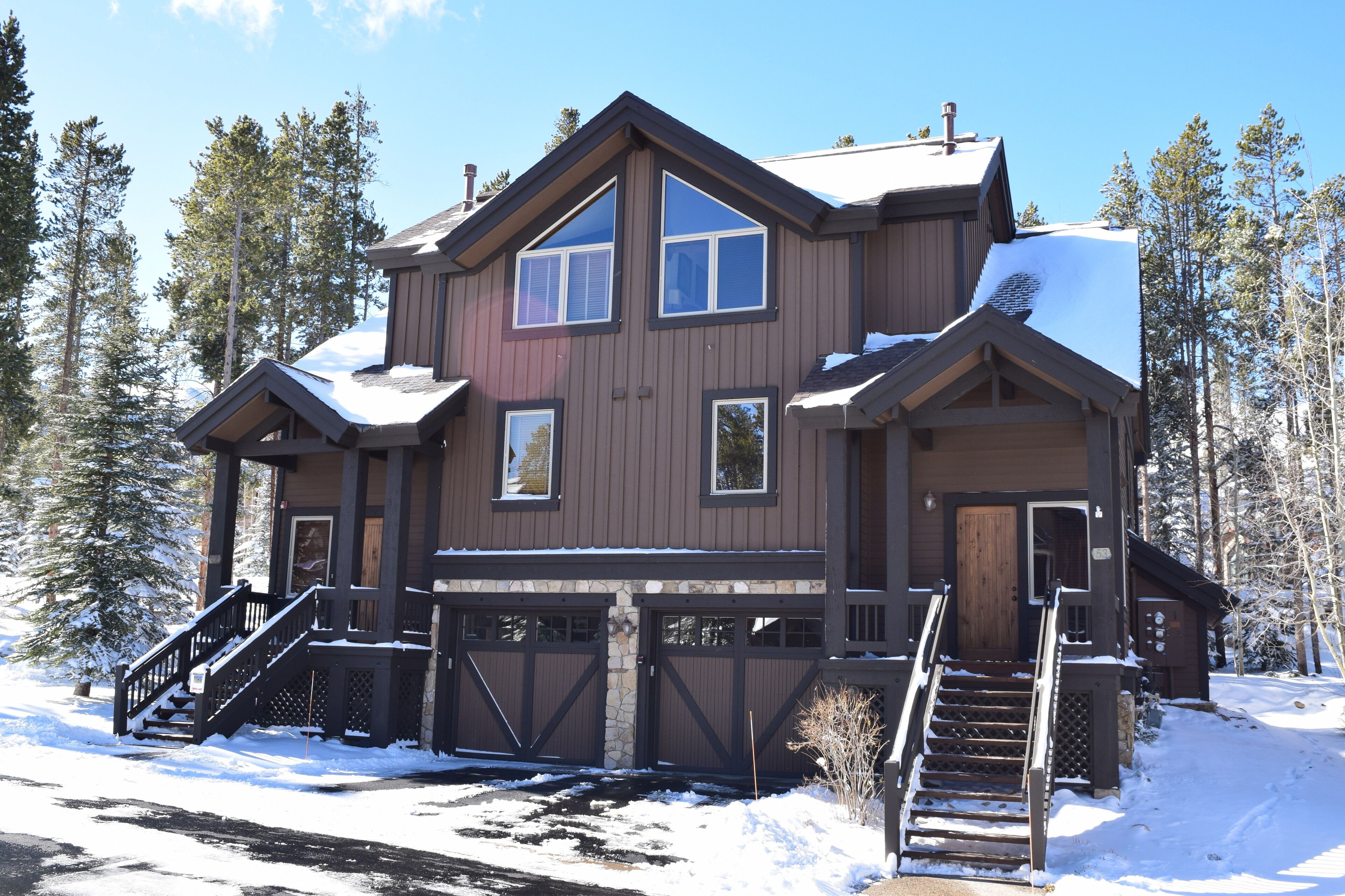 A two-story lodge with a stone foundation, a wooden deck, and a large garage.