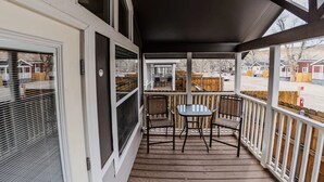 A covered porch with a table and chairs, large windows, and a view of a residential area.