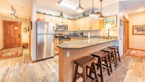 A kitchen with wooden cabinets, stainless steel appliances, a granite countertop, and bar stools.