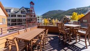 A wooden deck with tables and chairs, overlooking a mountainous landscape with buildings in the background.