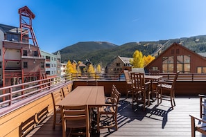 A wooden deck with tables and chairs, overlooking a mountainous landscape with autumn foliage.