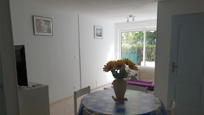 Un comedor con una mesa redonda cubierta por un mantel azul y blanco, rodeada de sillas blancas. Hay un jarrón con girasoles sobre la mesa.