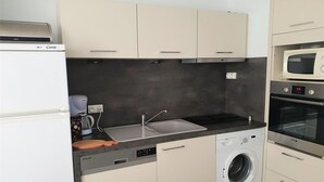 Una cocina compacta con lavadora integrada, microondas y cafetera.
