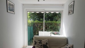 Una sala pequeña con un sofá, una mesita de centro y un ventanal corredizo que da a un jardín.