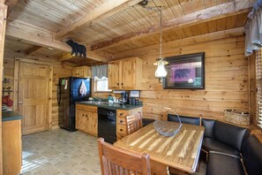 Cozy cabin-style kitchen and dining area features a wooden dining table, cabinetry, and a black refrigerator.
