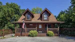 A two-story log cabin with a front porch, a flag, and a sign indicating it is a historic site. - ER100 - Making Memories  Great location - Close to town! (Pigeon Forge)