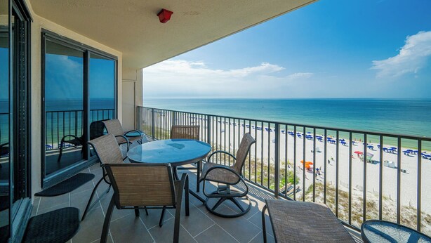 A balcony with a glass door leading to a beach view, furnished with chairs and a table. - Phoenix X 809 - Lovely 3BR Gulf Front Unit (Orange Beach)