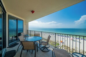 A balcony with a glass door leading to a beach view, furnished with chairs and a table.