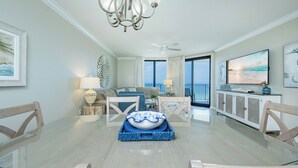 A spacious dining area with a glass table, a chandelier, and a view of the ocean through large windows. - Phoenix X 809 - Lovely 3BR Gulf Front Unit (Orange Beach)