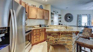 Una cocina con armarios de madera, una isla de piedra y un microondas.