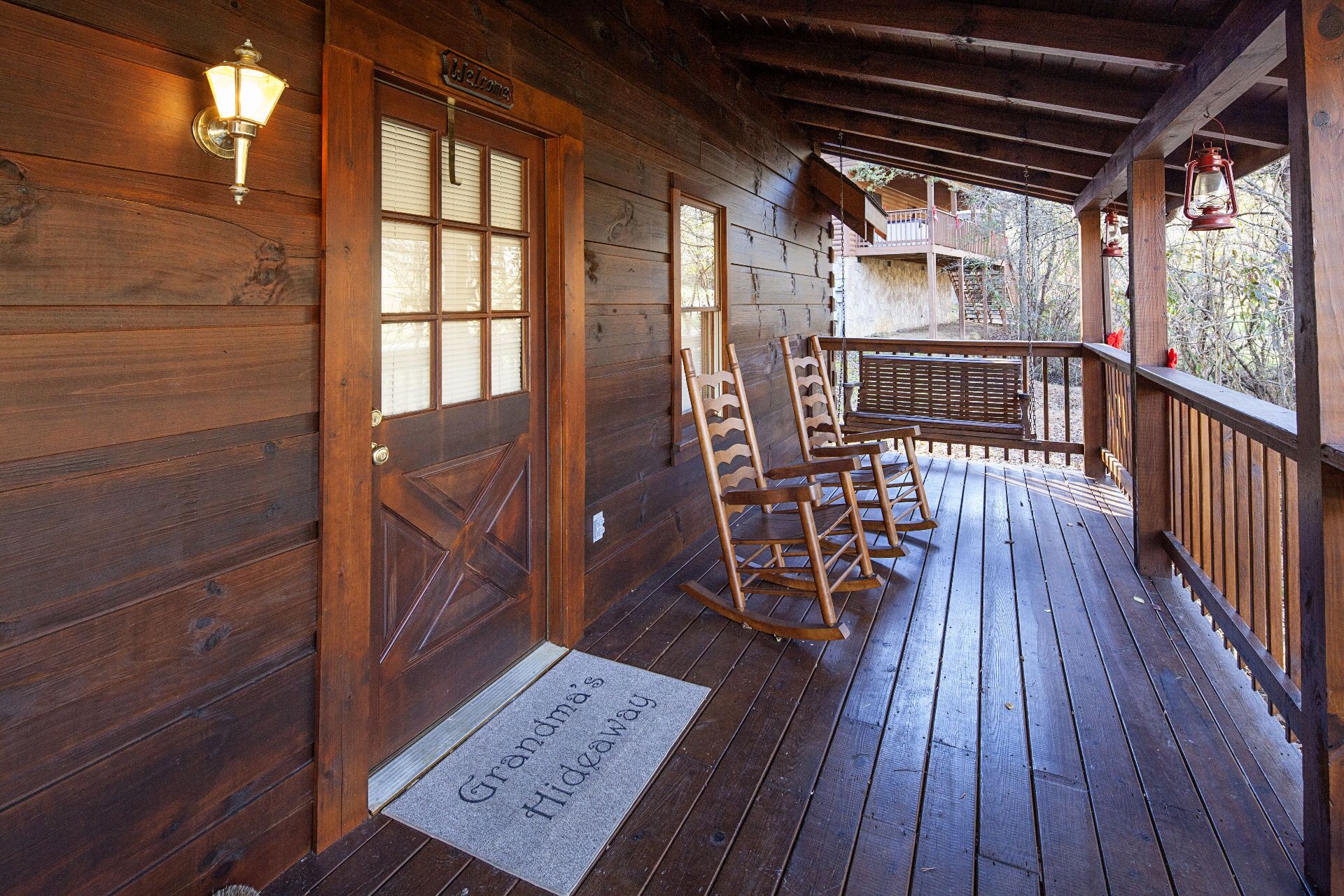 Une véranda en bois avec des fauteuils à bascule, une pancarte de bienvenue et un paillasson sur lequel on peut lire : « Le refuge de grand-maman ».