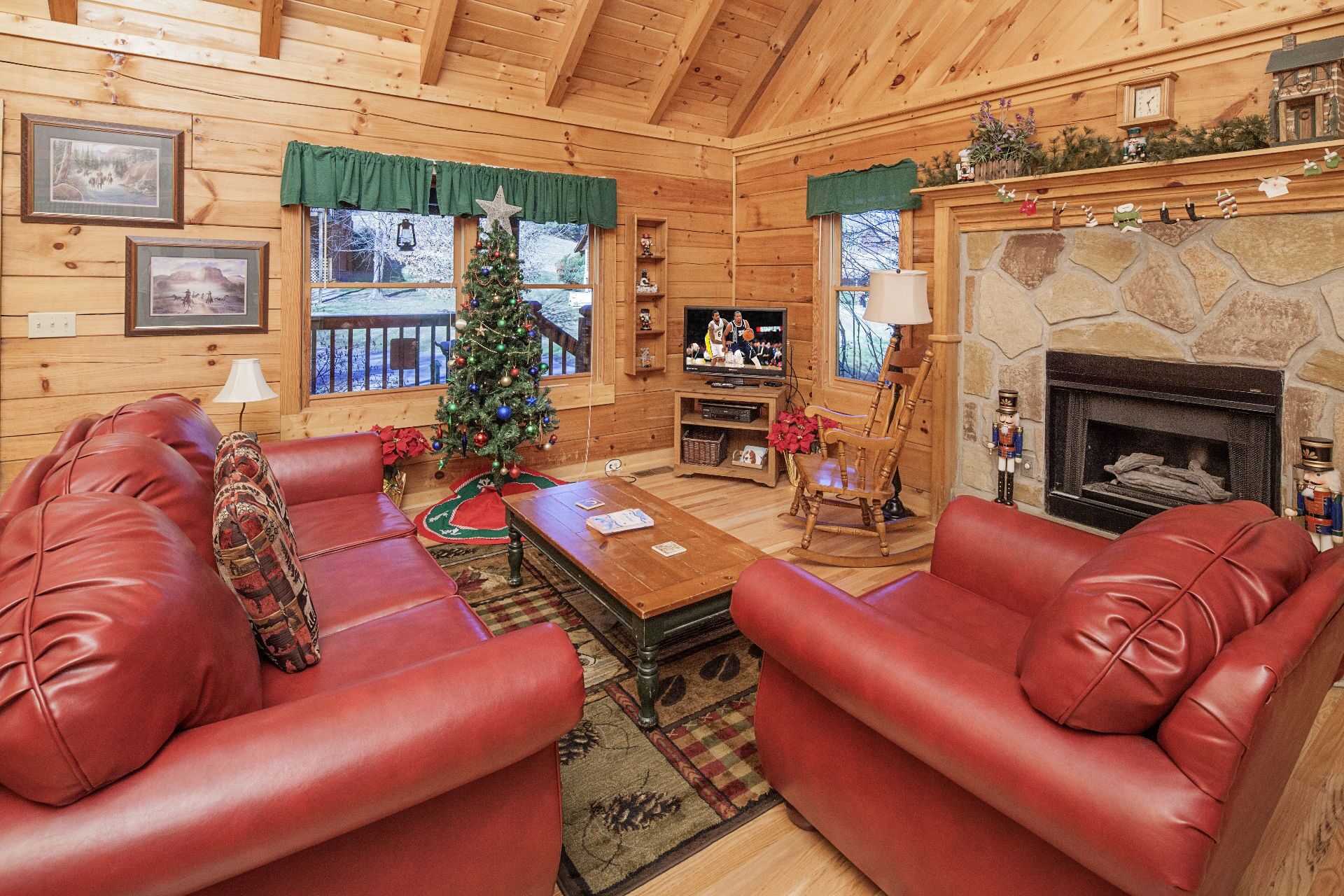 Un interior acogedor de cabaña de madera con sofás de cuero, un árbol de Navidad, una chimenea de piedra y un televisor.