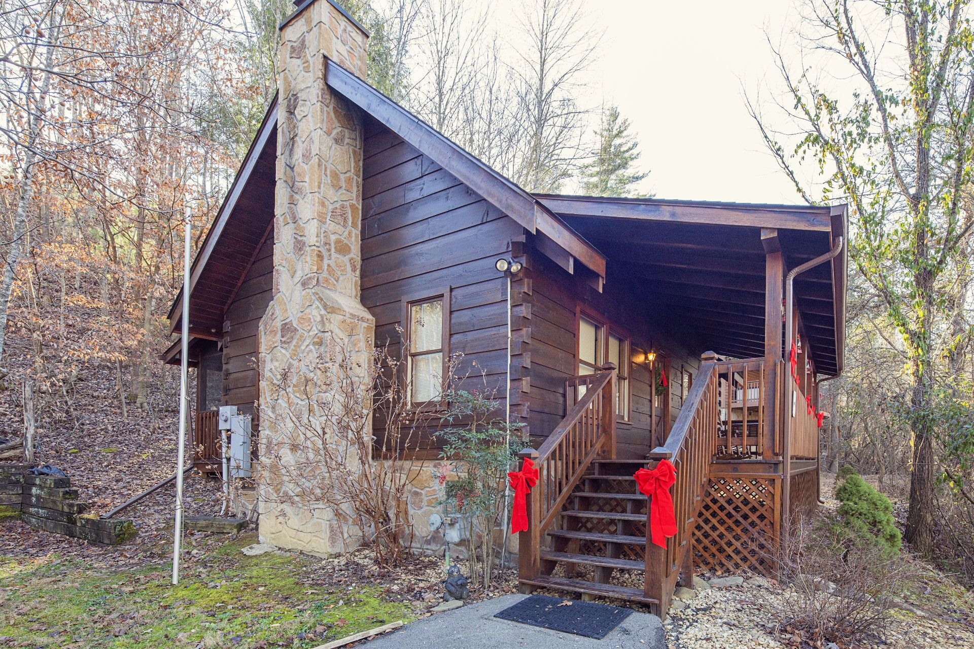 A rustic cabin with a stone chimney, wooden exterior, and a covered porch with red decorations.