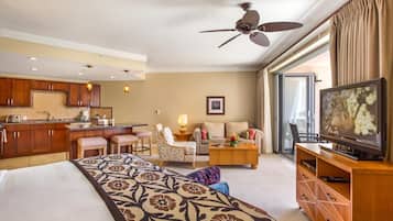 A hotel room with a bed, a sofa, a dining area, a TV, and a ceiling fan.
