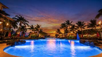 A swimming pool with a sunset view, surrounded by palm trees and hotel buildings.