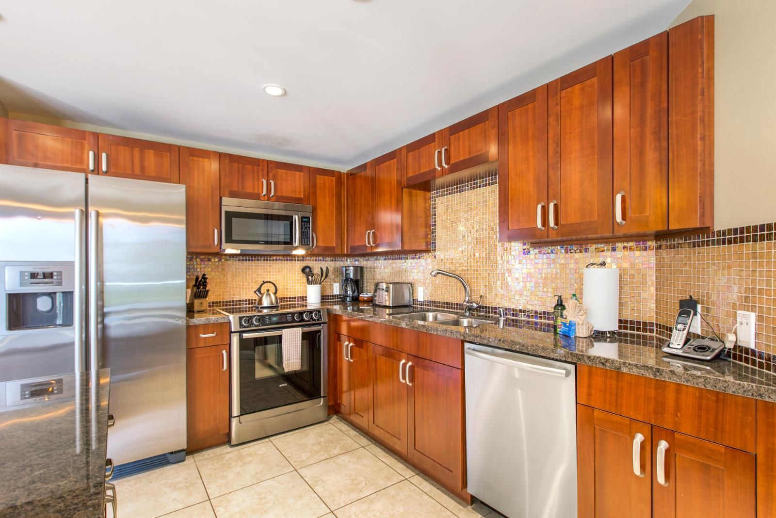 A modern kitchen with wooden cabinets, stainless steel appliances, a tiled backsplash, and a granite countertop.