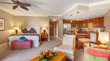 A hotel room with a bed, a desk, a chair, a coffee table, a kitchenette, and a ceiling fan.