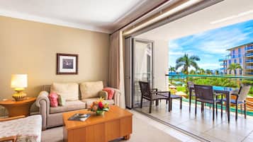 A hotel room with a sofa, coffee table, and a balcony with outdoor furniture.