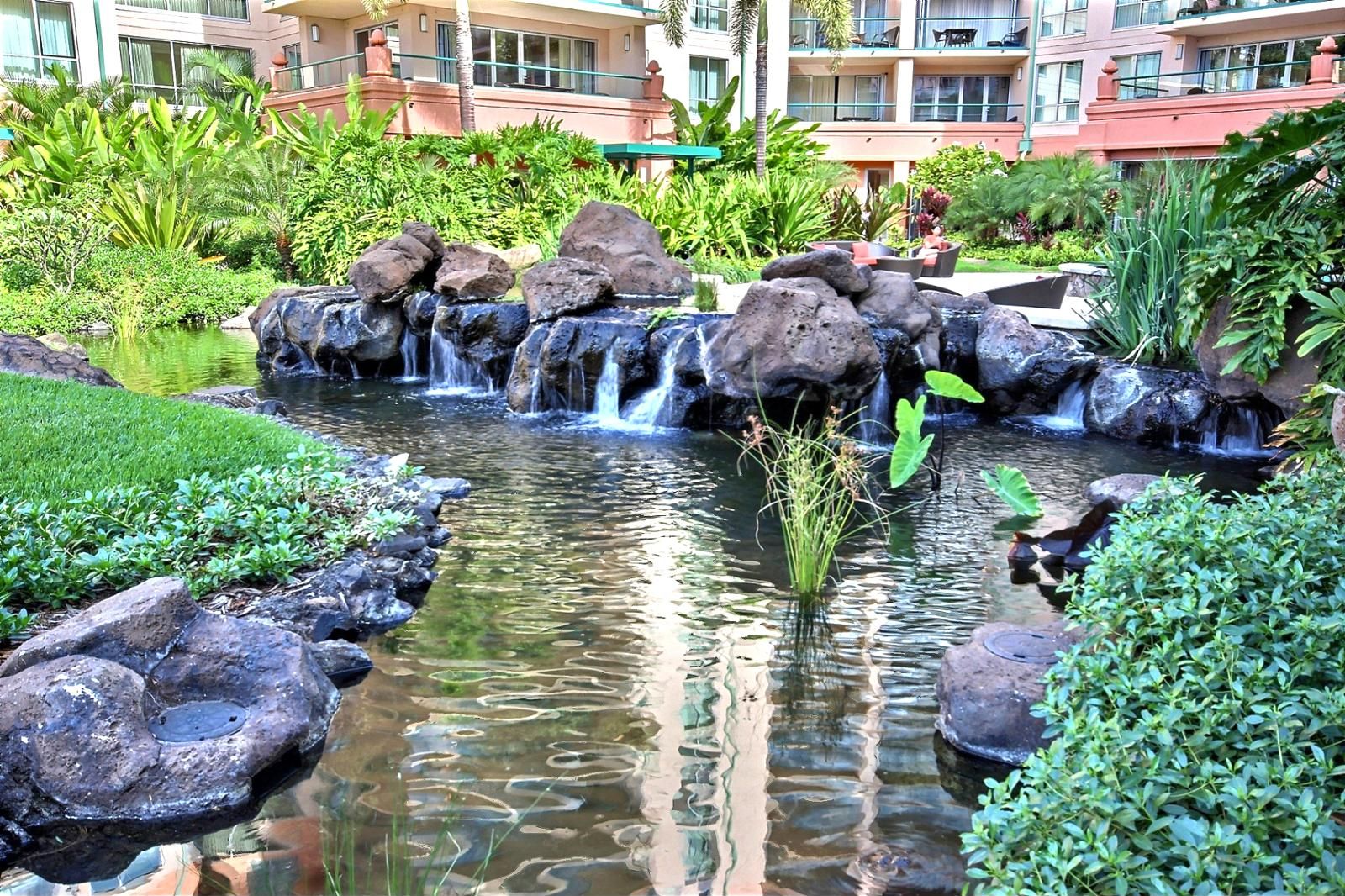 A landscaped garden with a small waterfall, surrounded by rocks and lush greenery.