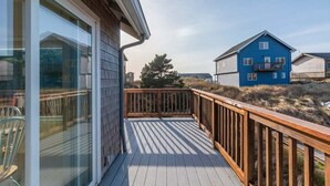 A wooden deck with a glass door leading to a room, overlooking a blue house and a grassy area.