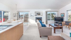 A spacious living area with a sofa, coffee table, TV, and a fireplace. There is a balcony with a railing and a dining area with chairs.