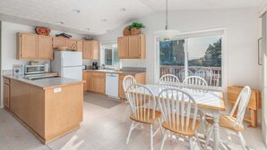 A modern kitchen with wooden cabinets, a central island, and a dining area with white chairs.