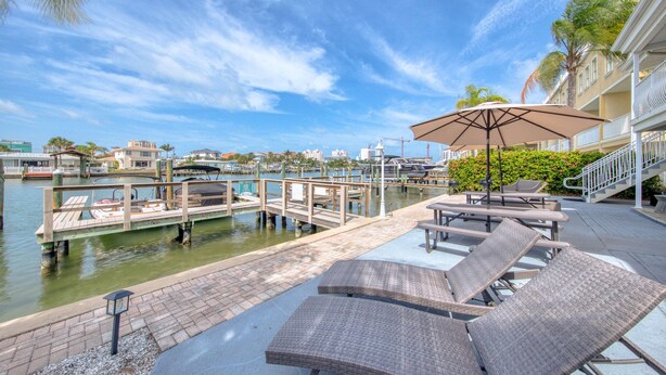 Une terrasse au bord de l’eau, dotée de chaises longues, d’une table avec un parasol et d’un quai où sont amarrés des bateaux.