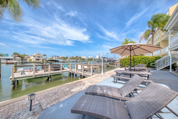 A waterfront patio with lounge chairs, a covered table, and a view of the marina.