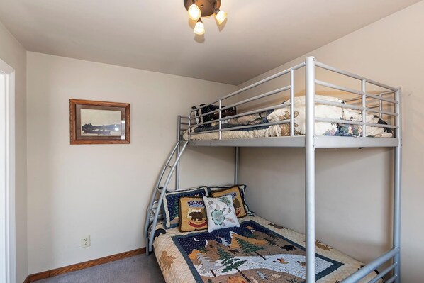 A bunk bed room with a ladder, a framed picture on the wall, and a quilt with animal prints.