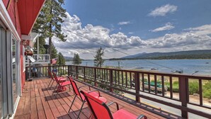 Terraza de madera con sillas rojas y vista a un lago y montañas.