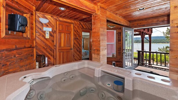 A wooden cabin with a hot tub, wooden walls, and a view of a lake.