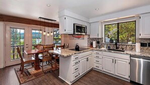 A modern kitchen with white cabinets, a stainless steel sink, and a large window offering a view of greenery.