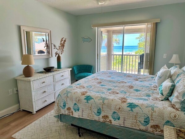 A bedroom with a bed, a dresser, a chair, and a view of the ocean.
