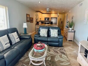A living room with a dark leather sofa, a coffee table with a decorative bowl, and a kitchen in the background.