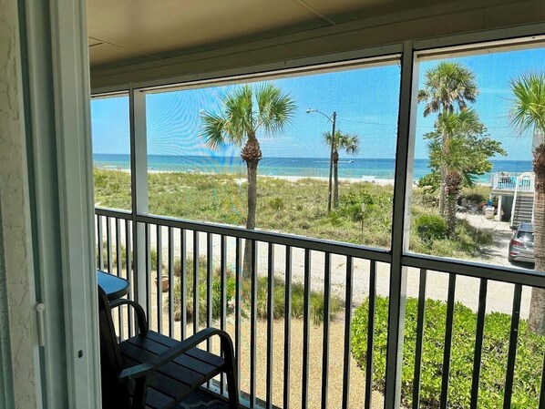 A balcony with a view of the beach and ocean, featuring palm trees and a parked car.