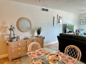 A living room with a dining table, chairs, a sofa, a TV, and a decorative mirror.